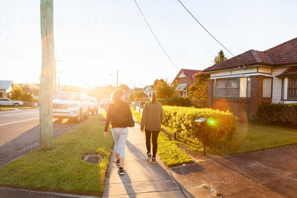 Two women walking down sunlit suburban road in Newcastle on bright afternoon - Australian Stock Image