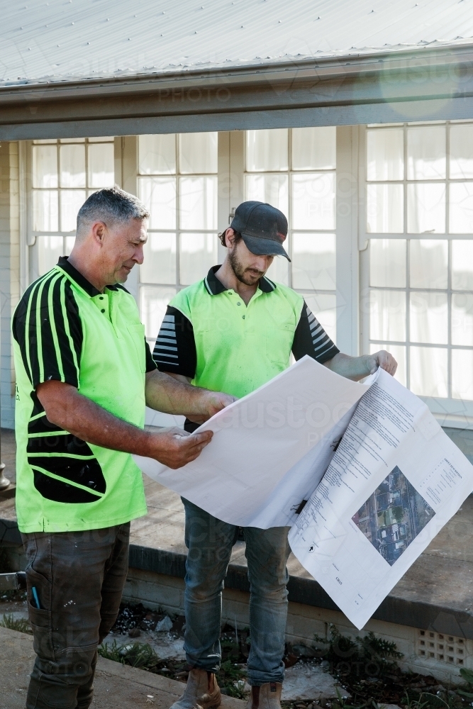Two workers discussing building plans at a construction site - Australian Stock Image