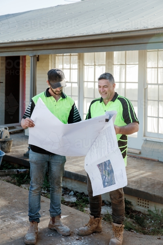 Two workers discussing building plans at a construction site - Australian Stock Image