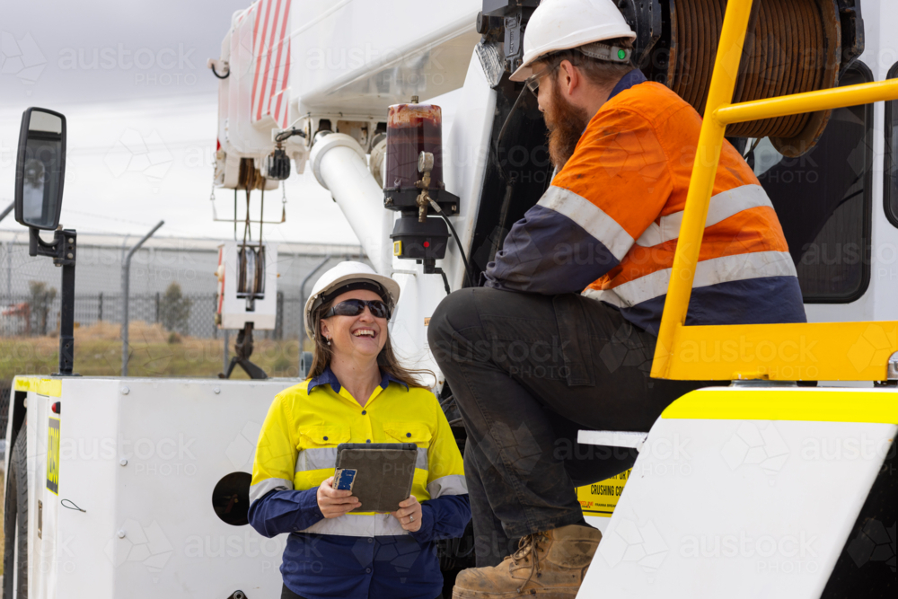 Two workers wearing high visibility clothing man sitting on the truck while woman showing the tablet - Australian Stock Image