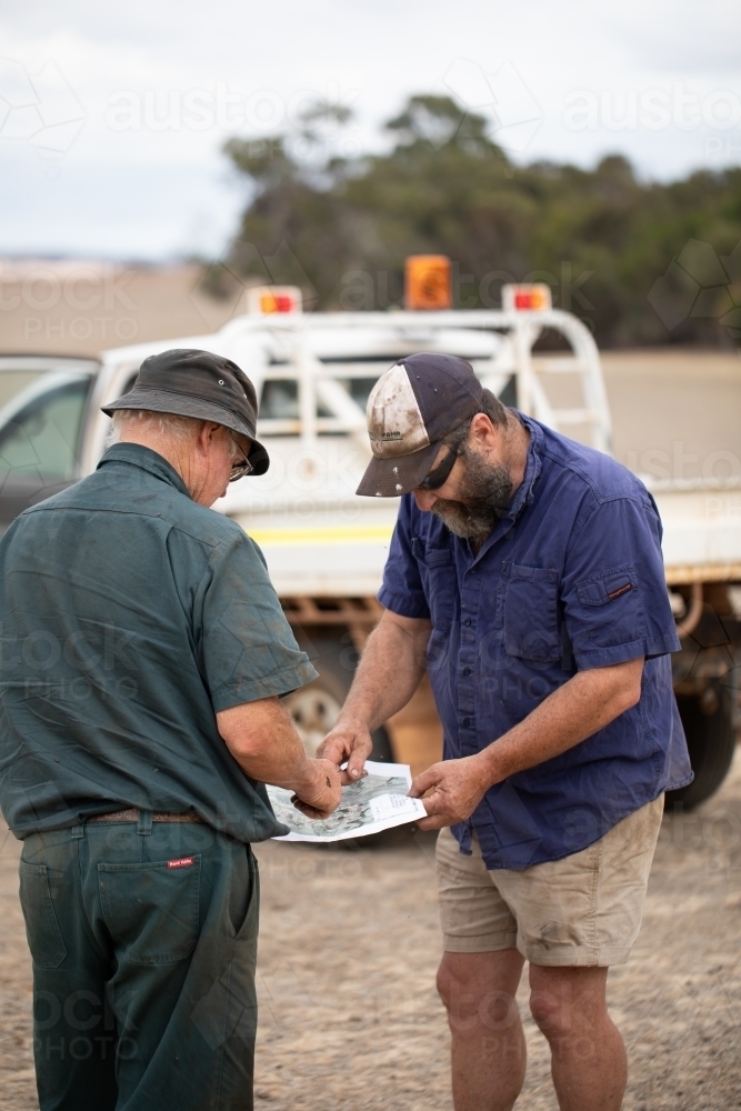two working men in the country looking at a map outdoors - Australian Stock Image