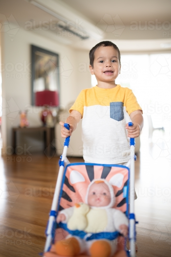 Two year old boy pushing toy stroller with a doll - Australian Stock Image