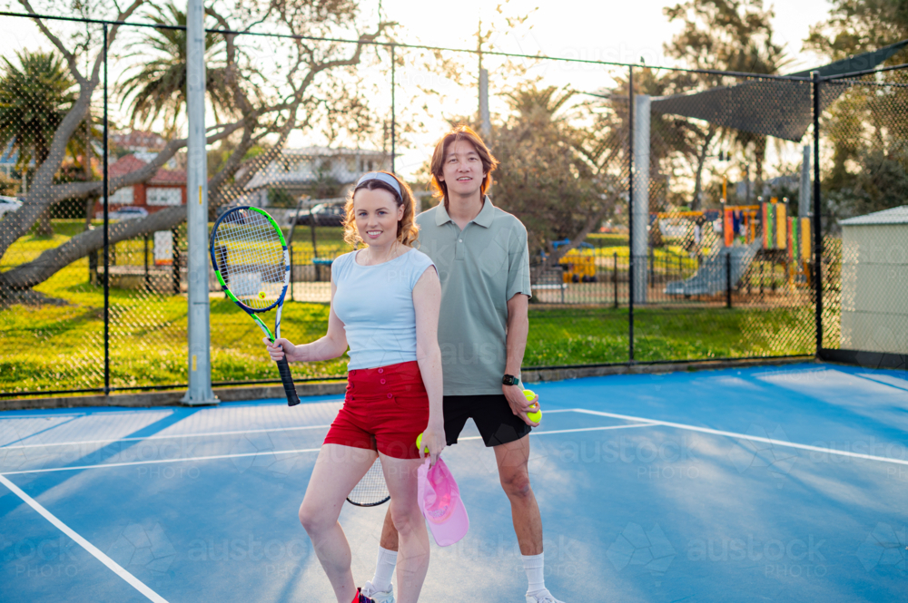 Two young adults prepare for a tennis match under the bright sun in a park - Australian Stock Image