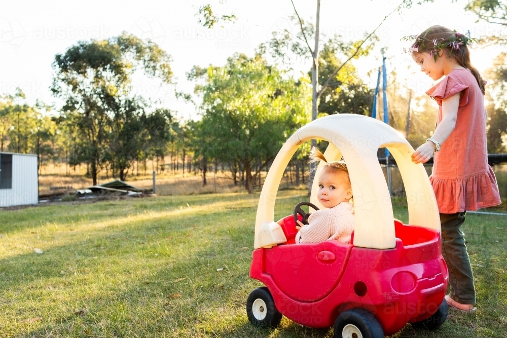 Two young aussie girls playing in rural backyard with plastic push car Cozy Coupe - Australian Stock Image