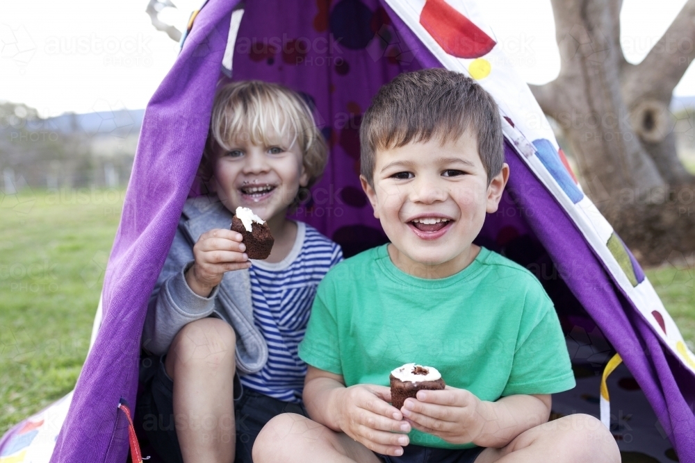 Two young boys eating cupcakes and smiling looking straight into the camera - Australian Stock Image