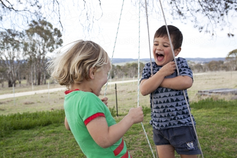 Two young boys having fun on tyre swing in country back yard - Australian Stock Image