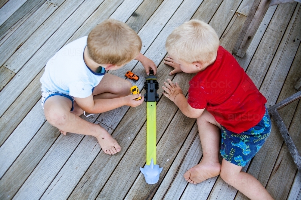 Two young boys play with cars on wooden decking viewed from above. - Australian Stock Image