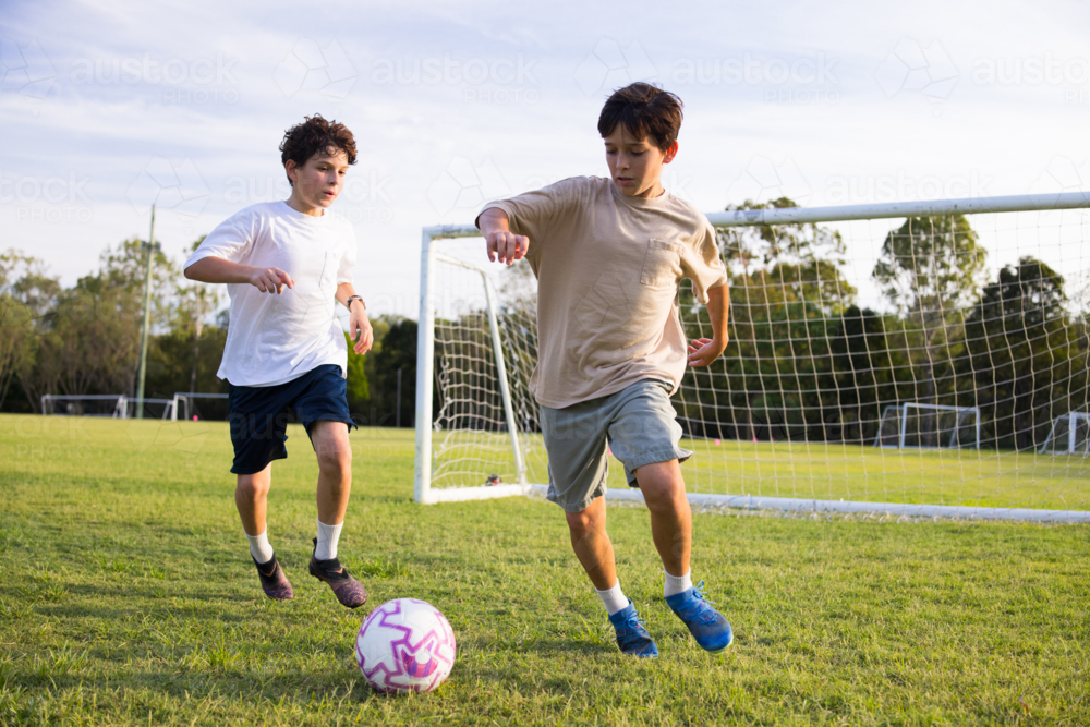 Two young boys playing soccer on grassy field near soccer goal - Australian Stock Image