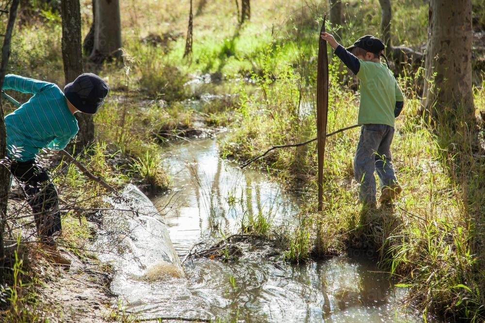 Two young boys playing with sticks in a creek - Australian Stock Image