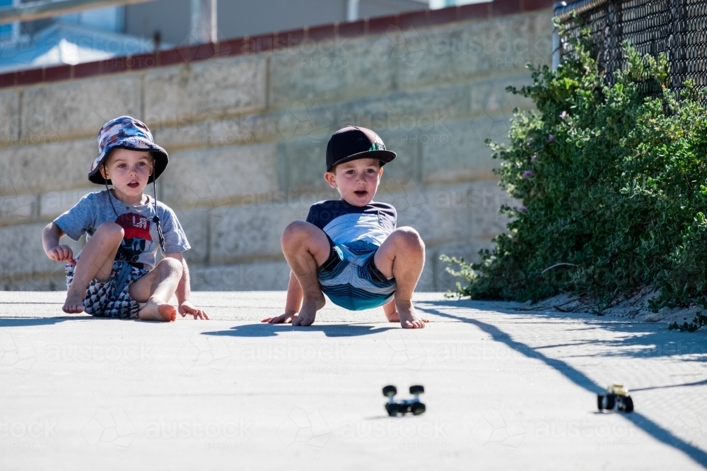 Two young boys racing toy car down embankment - Australian Stock Image