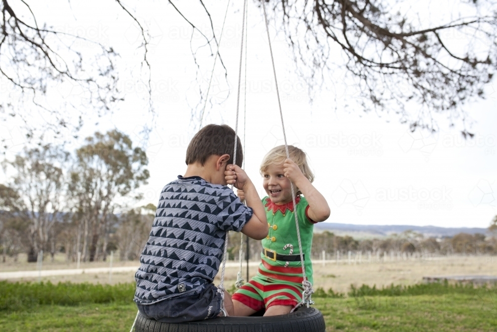 Two young boys sitting on tyre swing in country back yard - Australian Stock Image