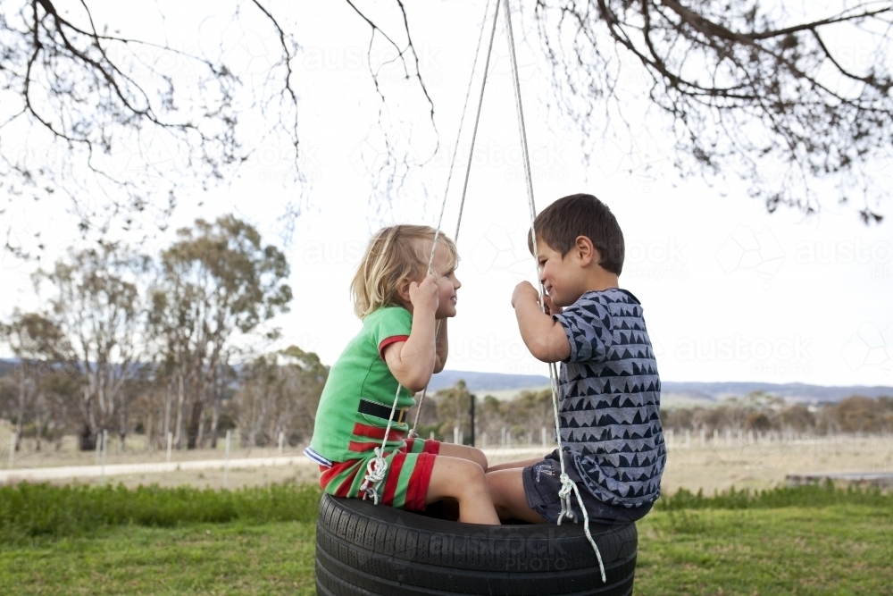 Two young boys sitting on tyre swing looking at each other - Australian Stock Image