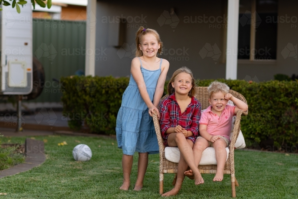 two young children sitting in a chair with another standing - Australian Stock Image