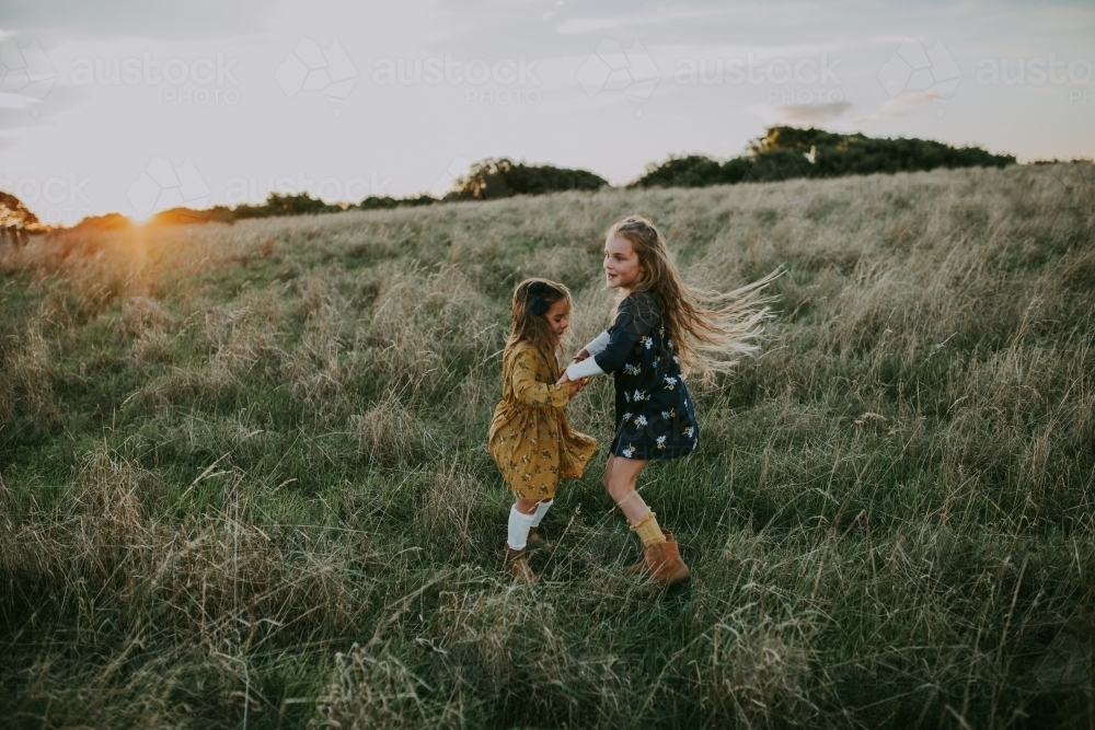 Two young fashionable sisters playing in a paddock at sunset - Australian Stock Image