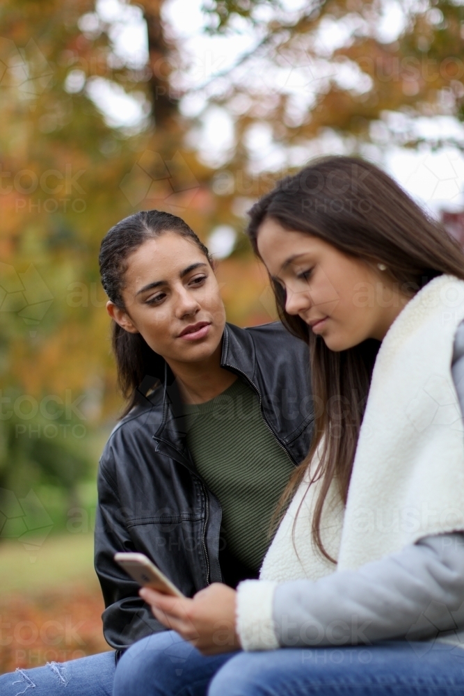 Two young female friends sitting together in an outdoor setting - Australian Stock Image