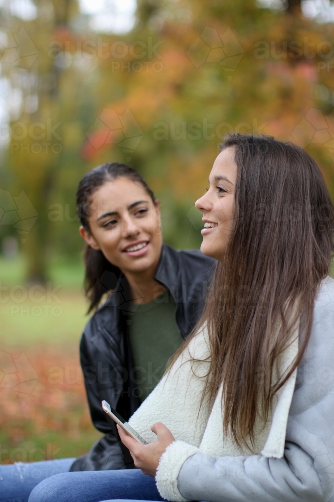 Two young female friends sitting together in an outdoor setting - Australian Stock Image