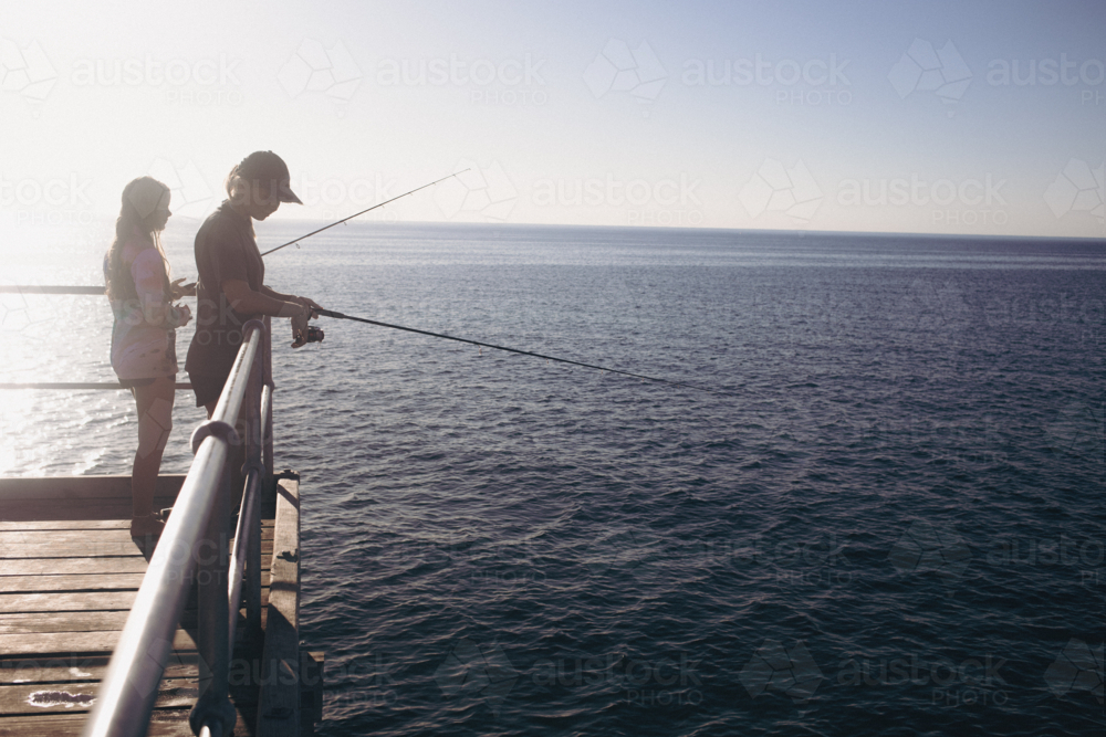 Two young female teenagers fishing from Jetty into calm water - Australian Stock Image