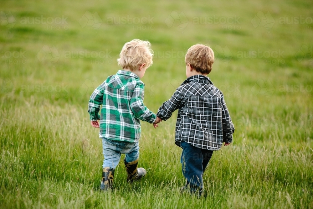 Two young friends walking across a green paddock - Australian Stock Image