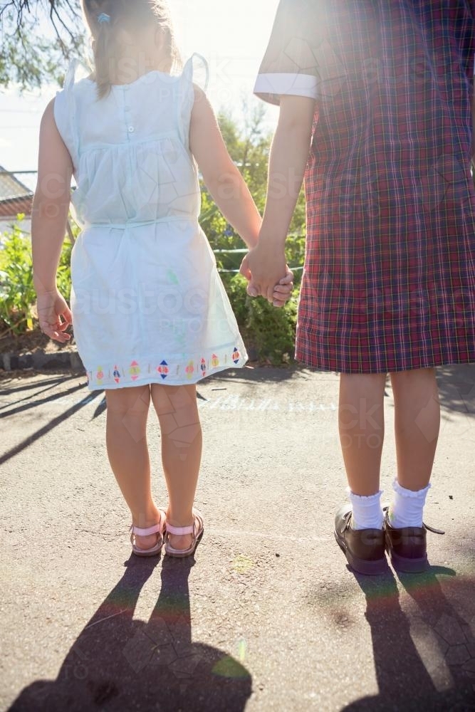 Two young girls holding hands with sun flare behind - Australian Stock Image