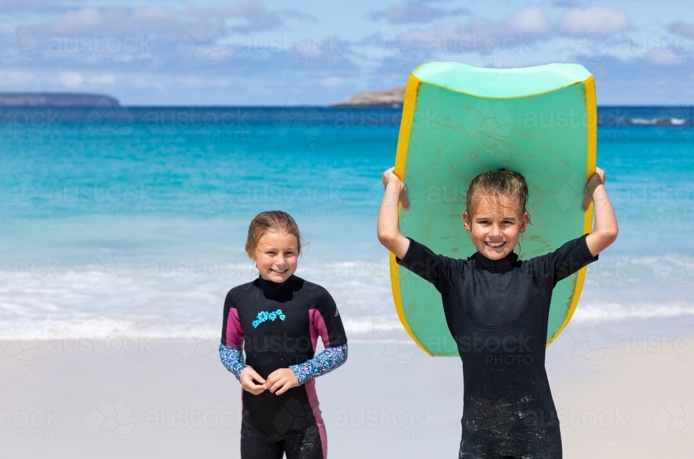 Two young girls in wetsuits on the beach with body board - Australian Stock Image