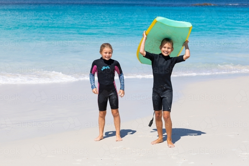 Two young girls in wetsuits on the beach  with body board - Australian Stock Image