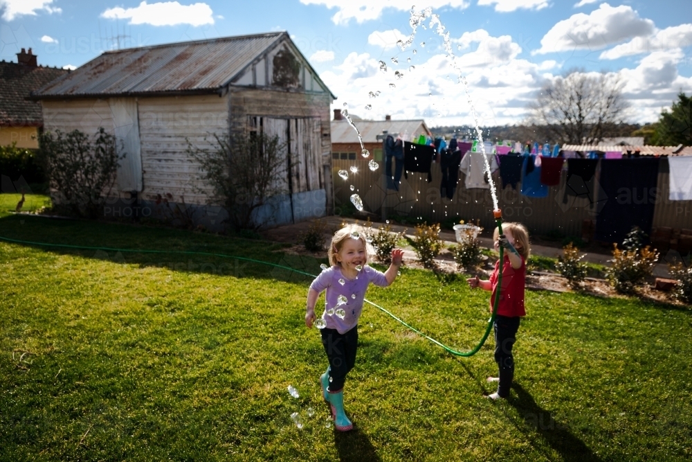Two young girls playing with a hose and water in the backyard - Australian Stock Image