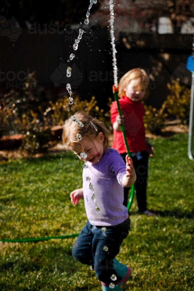 Two young girls playing with a hose and water in the backyard - Australian Stock Image