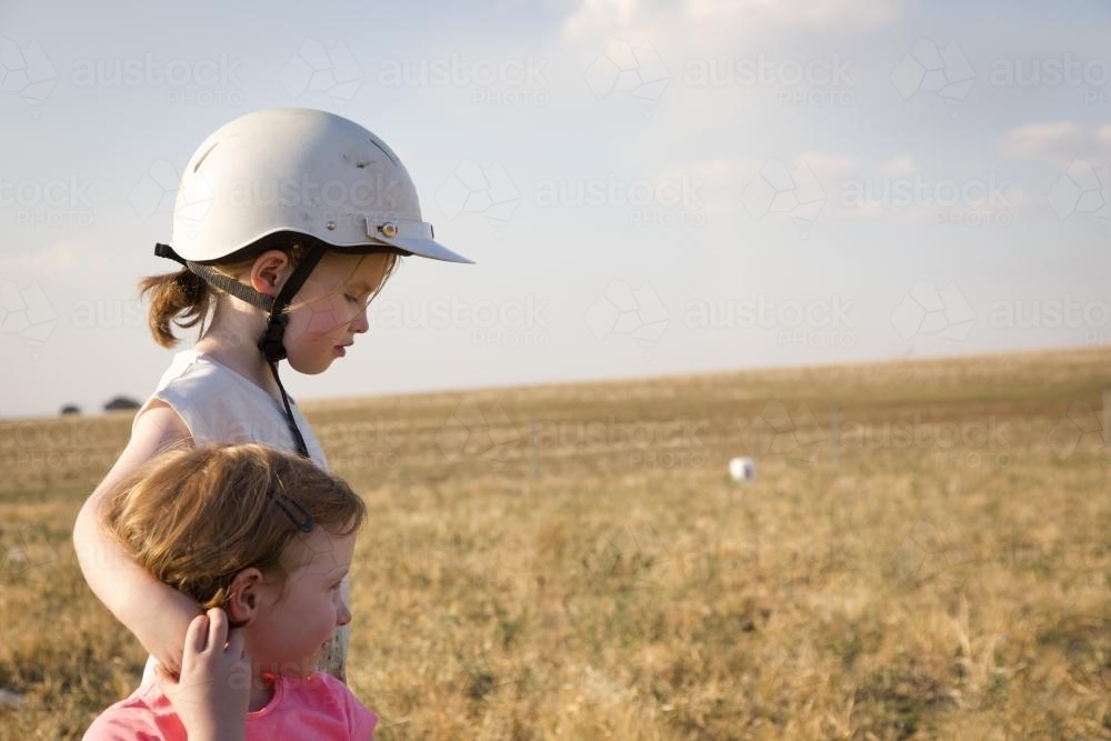 Two young girls (sisters) holding each other in a paddock - Australian Stock Image