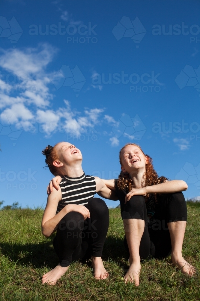 Two young girls sitting and laughing outside - Australian Stock Image