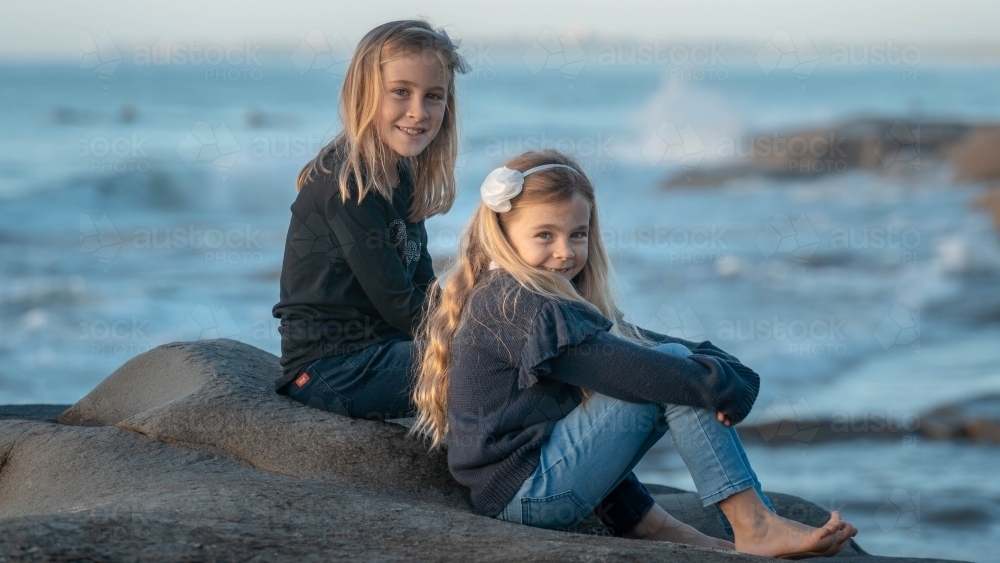 Two young girls sitting on rock at beach - Australian Stock Image