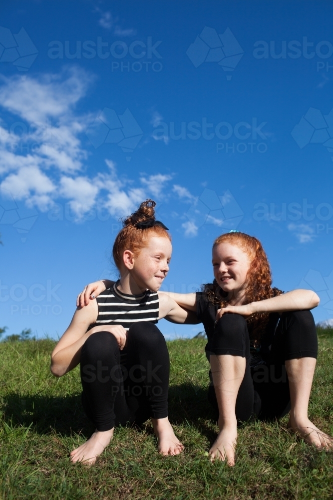 Two young girls sitting outside together - Australian Stock Image