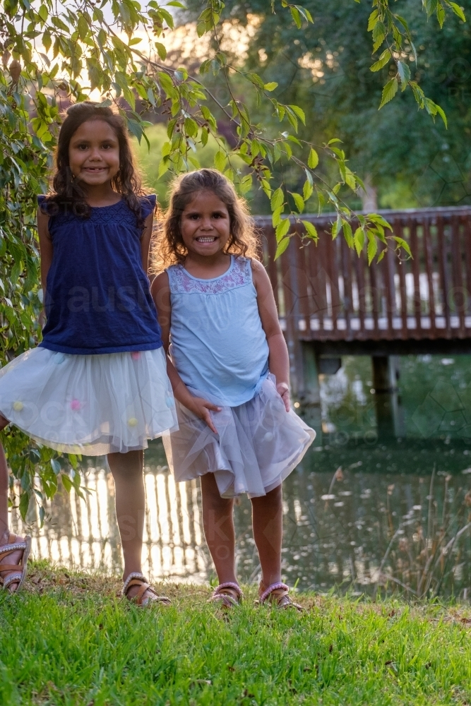 Two young girls standing on the grassy embankment of a dam in parkland - Australian Stock Image