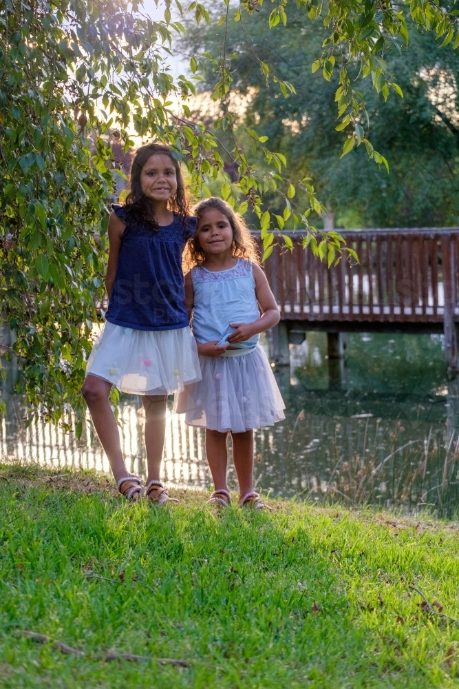 Two young girls standing on the grassy embankment of a dam in parkland - Australian Stock Image