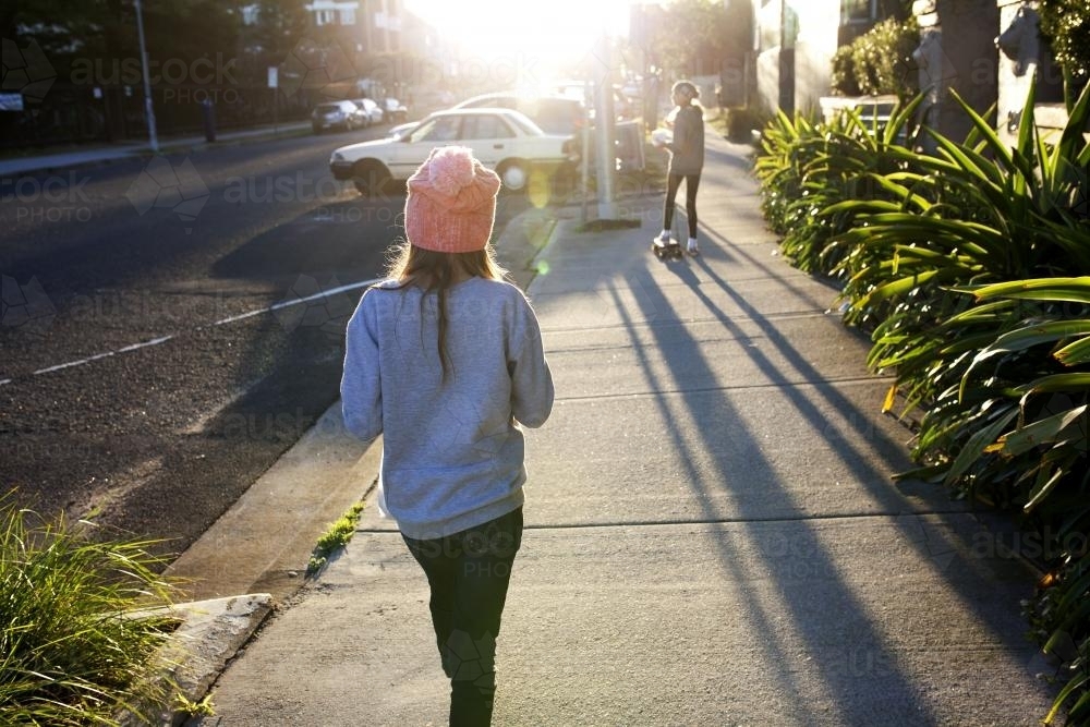 Two young girls walking away down a footpath in the afternoon light - Australian Stock Image