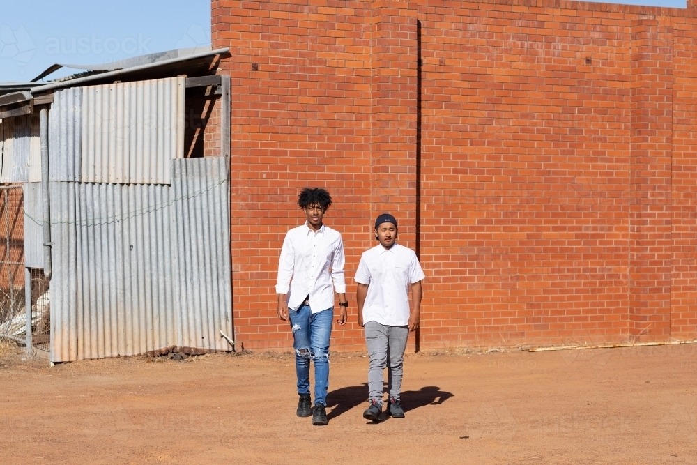 two young guys in jeans and white shirts outside - Australian Stock Image