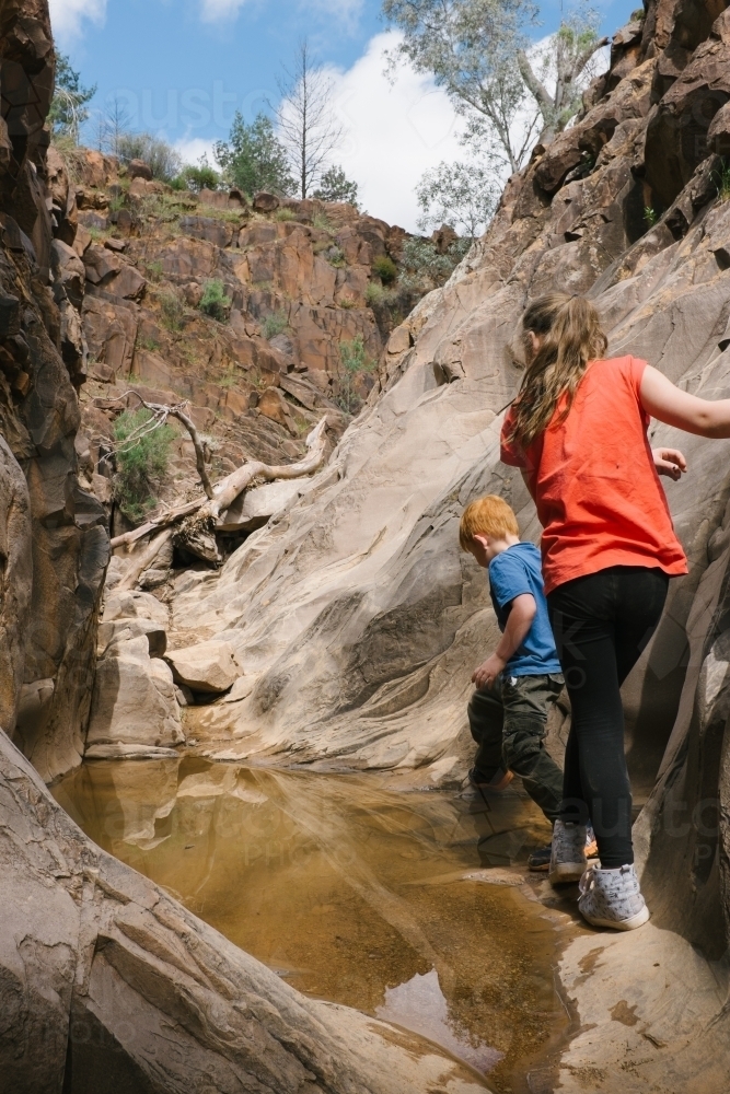 Two young kids climbing around a water filled canyon on a bush walk - Australian Stock Image