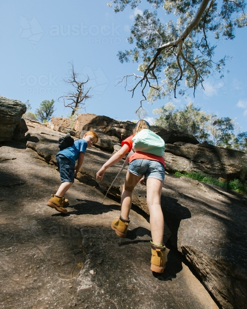 Two young kids completing a rocky climb during a bush walk - Australian Stock Image