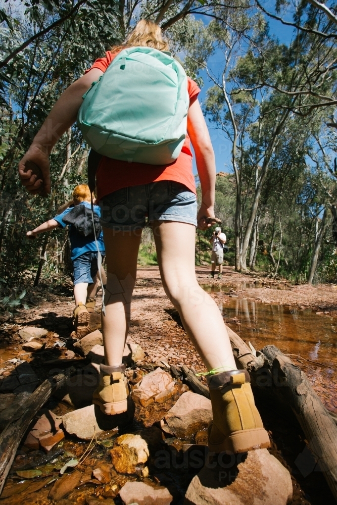 Two young kids crossing a creek during a bush walk - Australian Stock Image