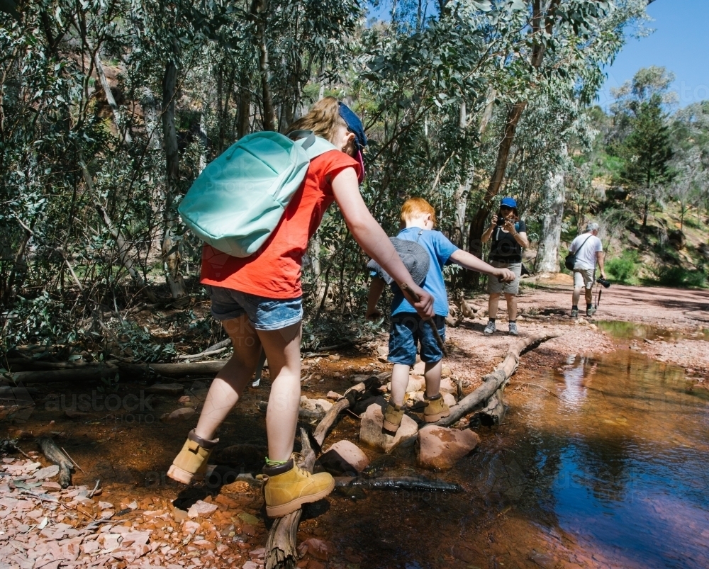 Two young kids crossing a creek during a bush walk - Australian Stock Image