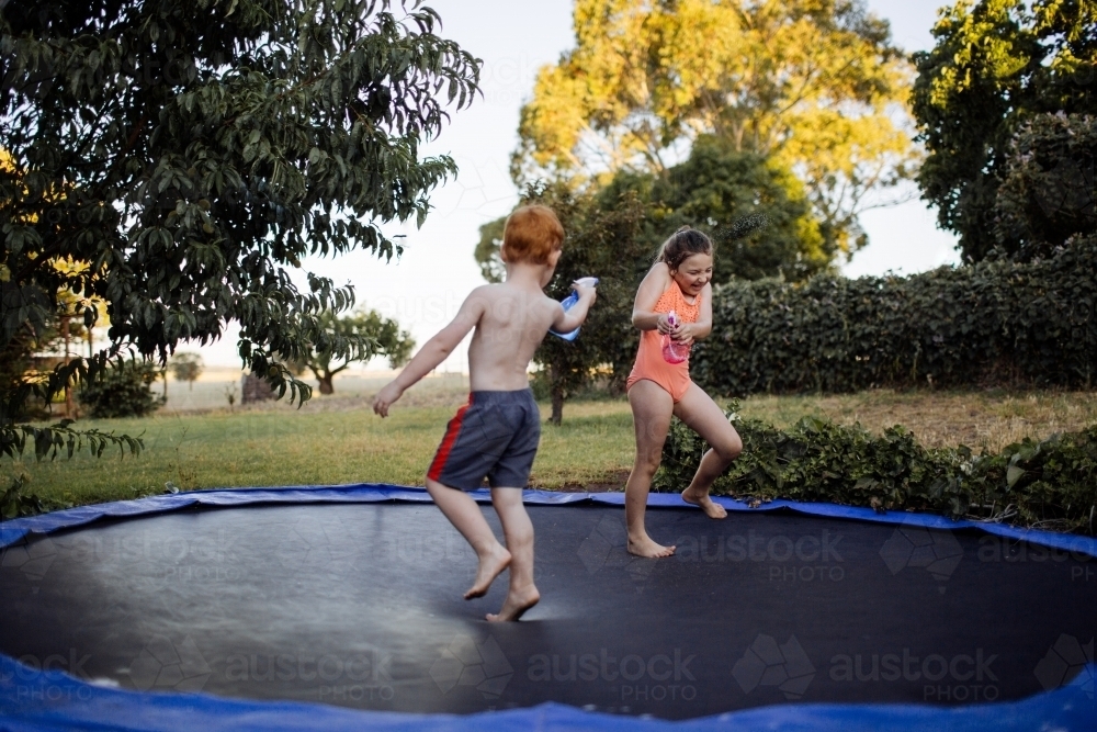 Two young kids having a water fight on a trampoline - Australian Stock Image