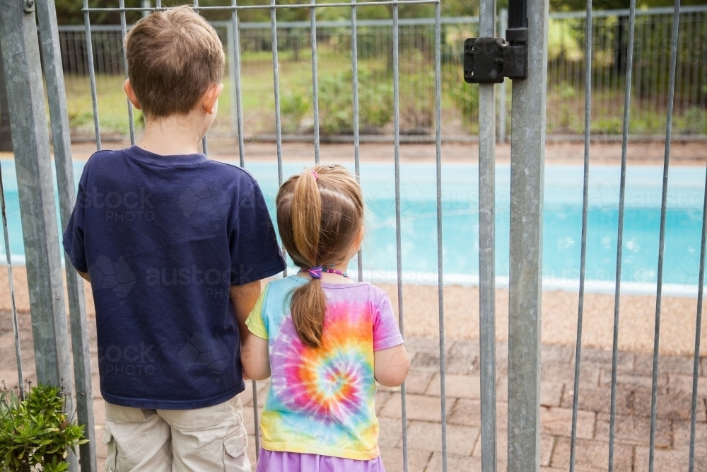 Two young kids looking through pool fence bars - Australian Stock Image