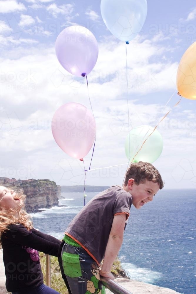 Two young kids with balloons by the ocean - Australian Stock Image