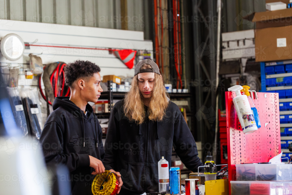 Two young male mechanics having a chat by workbench inside mechanics workshop - Australian Stock Image