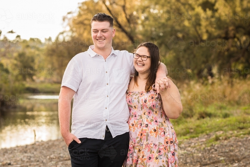 Two young people dating holding hands laughing as they look out over water - Australian Stock Image