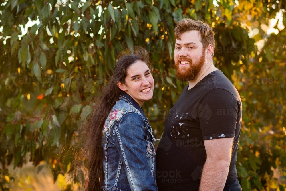 Two young people in their twenties smiling together in Australian bushland with gum leaves - Australian Stock Image
