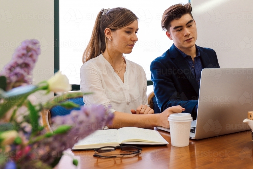 Two young professional office workers sitting at a meeting table with laptop : Austockphoto Two young professional office workers sitting at a meeting table with laptop - Australian Stock Image