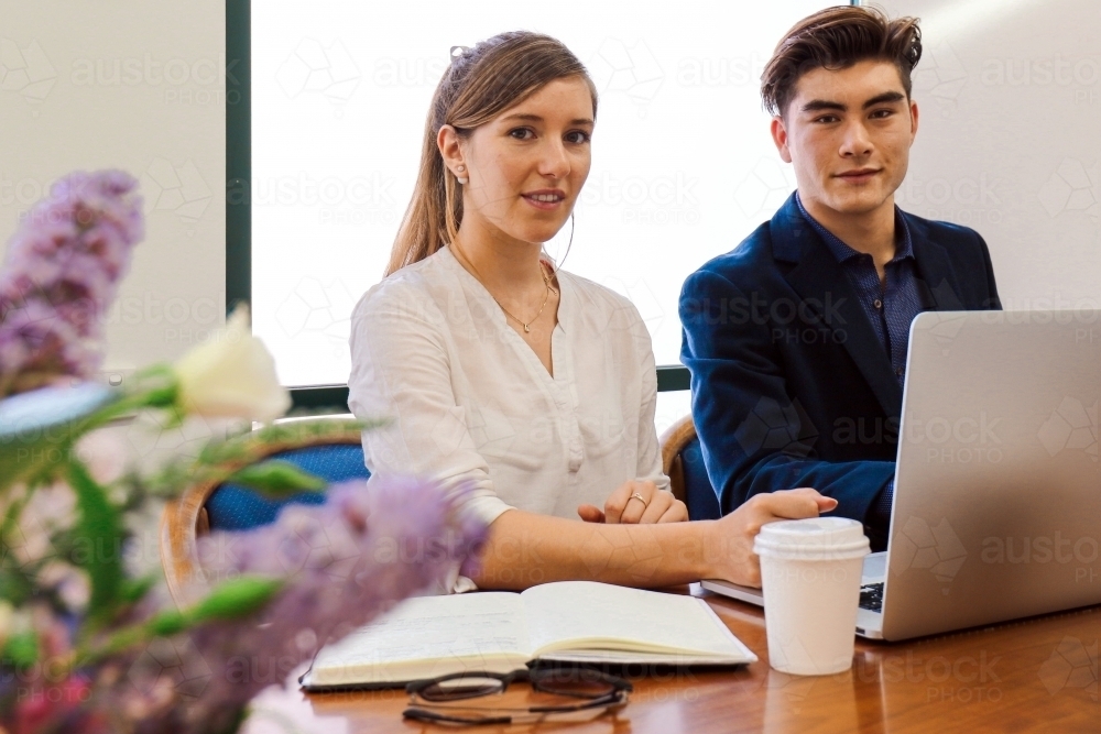 Two young professional office workers sitting at a meeting table with laptop - Australian Stock Image
