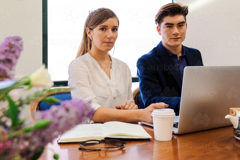 Two young professional office workers sitting at a meeting table with laptop - Australian Stock Image