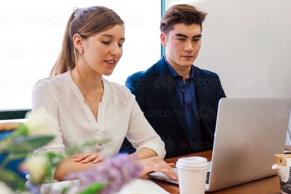 Two young professional office workers sitting at a meeting table with laptop - Australian Stock Image