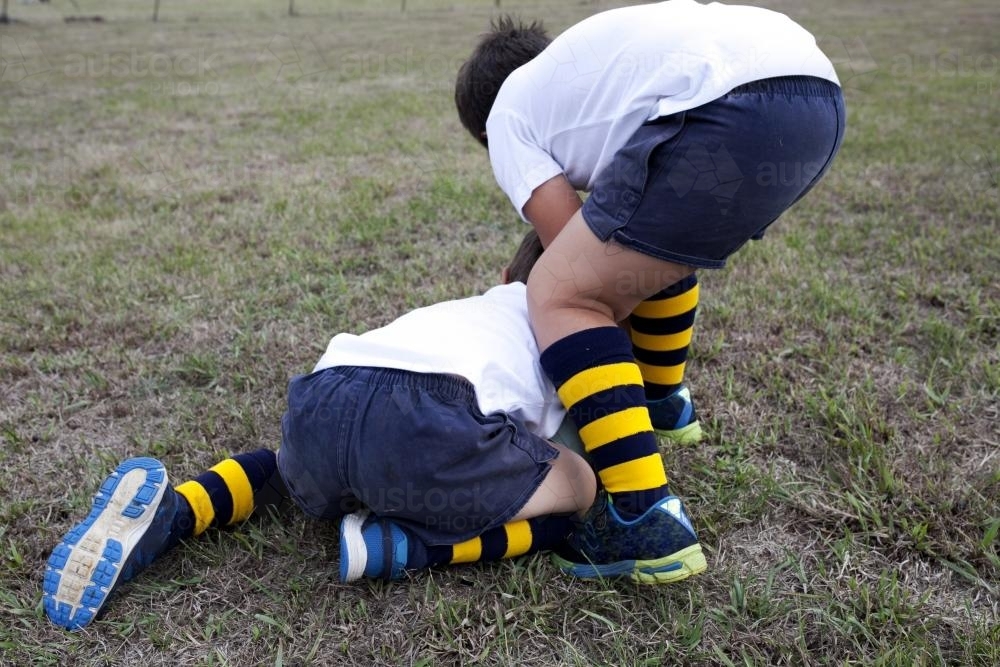 Two young school boys wrestling over a football - Australian Stock Image